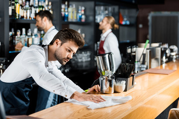 adult handsome barman cleaning wooden counter with cloth