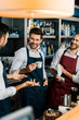 smiling barman drinking coffee and talking to colleagues at workplace