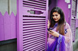 © AS Photo Family - Indian hindu girl at traditional violet saree posed at street against purple windows with mobile phone at hands.