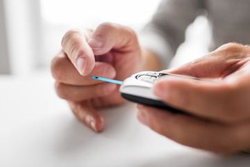 medicine, age, diabetes, health care and old people concept - senior man with glucometer checking blood sugar level at home