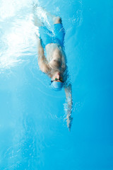 Wall Mural - Image on top of young sportsman in blue cap swimming on back in swimming pool