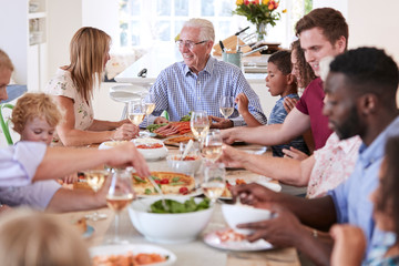 Wall Mural - Group Of Multi-Generation Family And Friends Sitting Around Table And Enjoying Meal