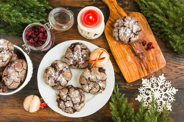 Wall Mural - Cracked chocolate cookies with cranberries on white plate on wooden rustic table. Christmas decoration, top view