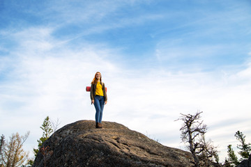 young tourist girl on huge rock with big puddle in the middle under beautiful blue sky enjoying fantastic view of mountains outstretched arms