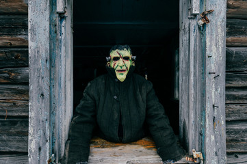 Wall Mural - Unknown person with creepy horrible latex mask looking out from old wooden ghost house window. Helloween concept.  Spooky terrible fearful monster. Children fear. Frightening tales. Nightmare.