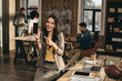 © LIGHTFIELD STUDIOS - smiling casual businesswoman holding smartphone with blank screen in loft office with colleagues working behind