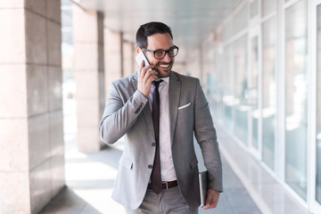 Close up of businessman dressed in formal wear using smart phone and holding tablet while walking on the street.