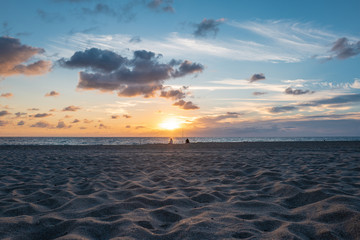 two distant fishermen at pompano beach at sunrise, view with sand in the foreground