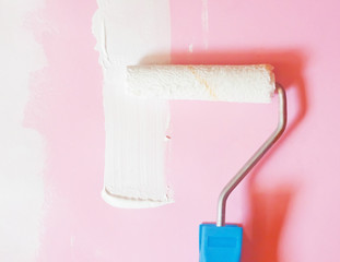 Roller with white paint next to the pink wall