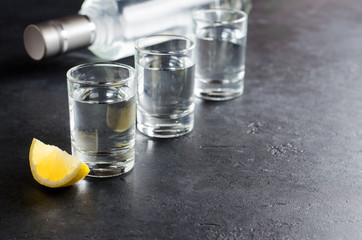 Wall Mural - Three glasses, a bottle of vodka, a piece of lemon on a dark background. Copy space