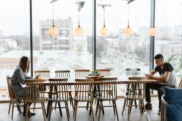 Two people a young man and a woman sitting at a big table, from different sides. distance between people. The concept modern problem personal communication