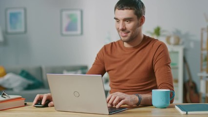 Wall Mural - Portrait of Handsome Smiling Man Working on Laptop, Sitting at His Wooden Desk at Home. Man Browsing Through Internet, Working on Notebook from His Living Room.