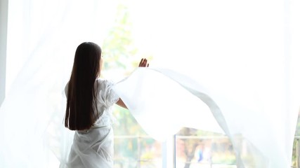 Canvas Print - Woman opening curtains at home on beautiful morning
