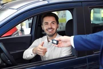 Wall Mural - Young salesman giving car key to client in dealership