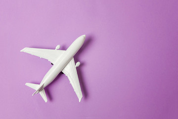 Simply flat lay design miniature toy model plane on violet purple pastel colorful paper trendy background. Travel by plane vacation summer weekend sea adventure trip journey ticket tour concept