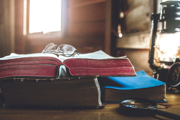 focus holy Bible and place eyeglass on book. with light of oil lamp at home. in morning. on wooden table.