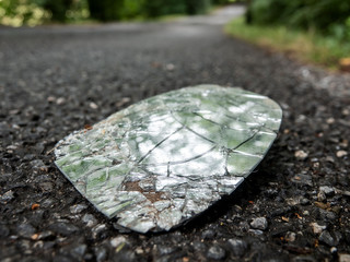 Broken shards of the rearview mirror of the car on an asphalt road