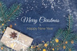 Merry Christmas and Happy New Year card with text, gift with anise star, fir branches, snowflakes and yellow lights on blue background, toned. Greeting concept, top view, layout design