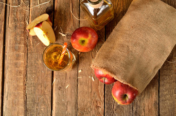 View from above of homemade apple juice with ice, red apples, straw, still life on a wooden table