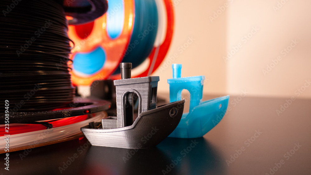 Two 3D printed boats on a black surface with 3D printer filament in the background. - obrazy, fototapety, plakaty 