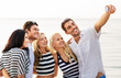 © Syda Productions - friendship, summer holidays and people concept - group of happy friends taking picture by smartphone on beach
