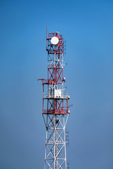 View of red and white communication tower against blue sky