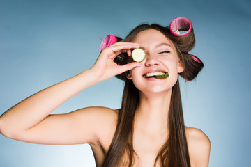 Poster - happy young girl takes care of herself, on the head of the curler, keeps the cucumber for moisturizing the skin of the face