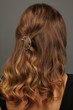 Close up isolated portrait of a lady with wavy ombre hair. The back view of the girl with half-up half-down hairstyle, adorned with silver crescent moon barrette. Posing over the grey background.