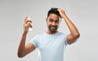 grooming, hairstyling and people concept - happy smiling indian man applying hair spray over grey background