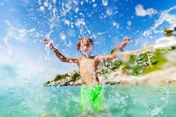 Wall Mural - Excited boy having fun splashing water in the sea