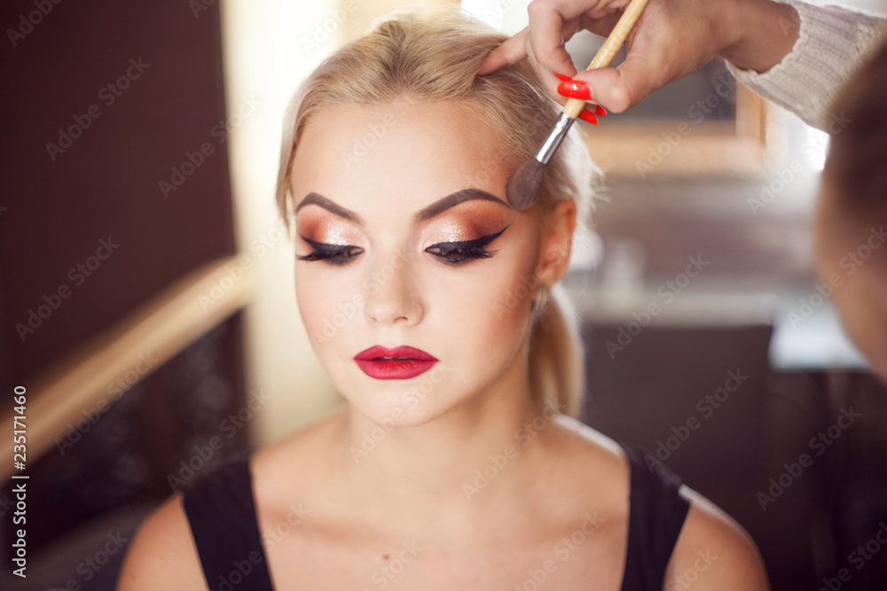 Beautiful young blonde. Makeup artist makes a stylish makeup. - obrazy, fototapety, plakaty 