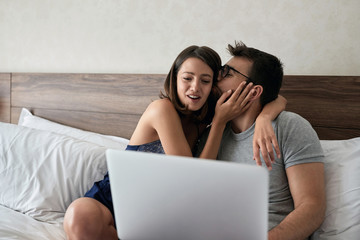 Wall Mural - happy couple using laptop together and kissing in bed at home in bedroom.