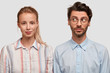 Photo of attractive blonde woman with pony tail, curious unshaven guy stand shoulder to shoulder against white background, have friendly relationships. Two colleagues meet together for making project