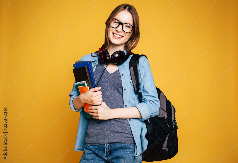 Happy and excited cute young student girl portrait in glasses with backpack isolated in studio - obrazy, fototapety, plakaty 
