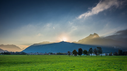 Wall Mural - volume light beams of sunset sun behind peak of mountain chain in austria holiday