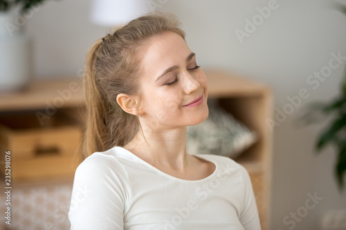 Cuadros en Lienzo Close up of happy young woman sitting with eyes closed dreaming at home, smiling