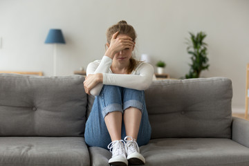 Unhappy female sit on sofa feeling lonely and sad, upset girl crying at home having relationships or life problems, hurt young woman on couch coping with emotions after breakup or bad news