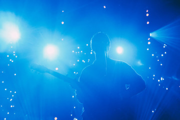 Canvas Print - Rock band front man silhouette on a stage with guitar singing to microphone in colorful backlights 