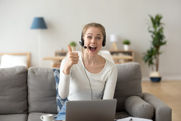Portrait of excited young female wearing headset show thumbs up to camera recommending online course or training, happy girl in earphones sit with laptop at home gesture liking educational program