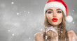 © Subbotina Anna - Christmas winter fashion girl on holiday blurred winter background. Beautiful New Year and Xmas holiday makeup. Beauty model woman in Santa's hat blowing snow in her hand