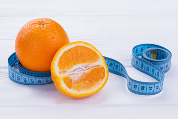 Close up fruits and measuring tape. Whole and half of orange fruits with tape measure on wooden background. Body fitness programm.