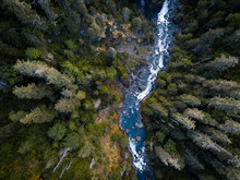 Aerial Drone View Looking Down At A Pristine Blue Mountain River Running Through The Tall Trees Of The Forest