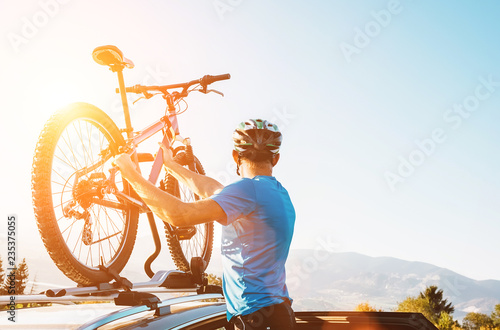 Fotografía Mountain biker man take of his bike from the car roof evening sunset image