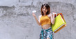 © kaew6566 - Joyful young woman holding shopping bags and blank credit card on concrete walls background with copy space. Happiness, consumer, sale and people concept.