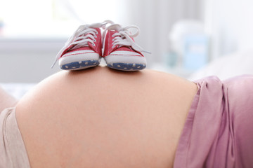 Poster - Pregnant woman with baby booties on blurred background, closeup view