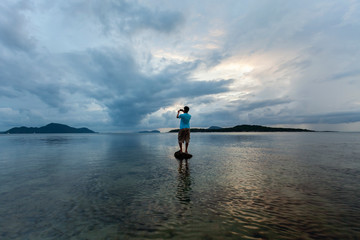 Alone man tourist standing on the stone in tropical sea and enjoying scenery during sunrise or sunset beautiful light dramatic sky environment in phuket thailand.