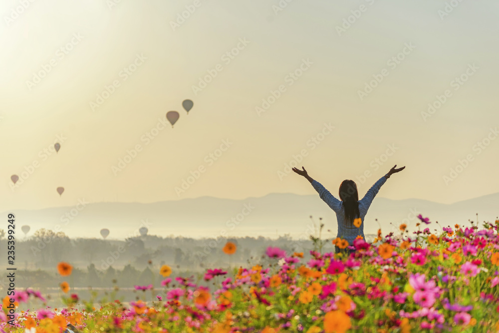 Lifestyle traveler women raise hand feeling good relax and happy freedom and see the fire balloon on the nature tea and cosmos farm in the sunrise morning. Travel and summer Concept - obrazy, fototapety, plakaty 
