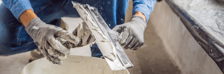 master is applying white putty on a wall and smearing by putty knife in a room of renovating house in daytime BANNER, long format