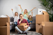 © snedorez - Picture of upset man sitting on floor and happy women with boy and girl sitting on gray sofa among cardboard boxes