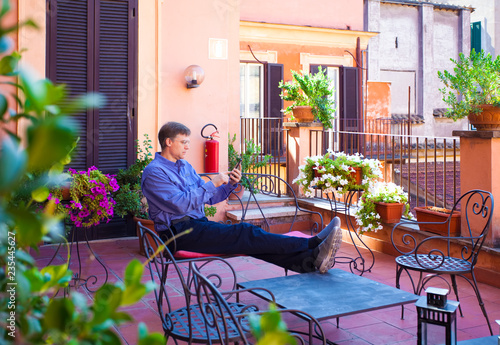 Fotografie, Obraz Caucasian man sitting on Italian veranda looking at cellphone